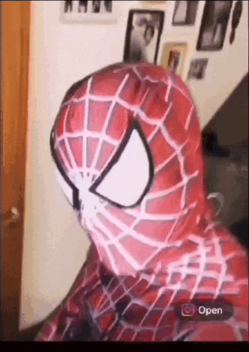 a person in a spiderman costume is sitting in front of a wall with pictures on it .
