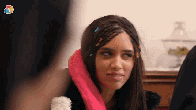 a woman with braids and a pink scarf on her neck looks at the camera