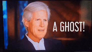 a man in a suit is on a tv screen with the words a ghost behind him