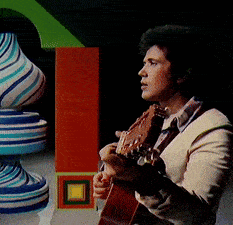 a man playing a guitar in front of a colorful sculpture