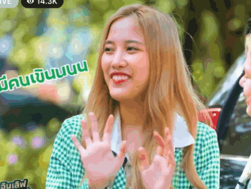 a woman in a green and white plaid shirt is smiling and waving