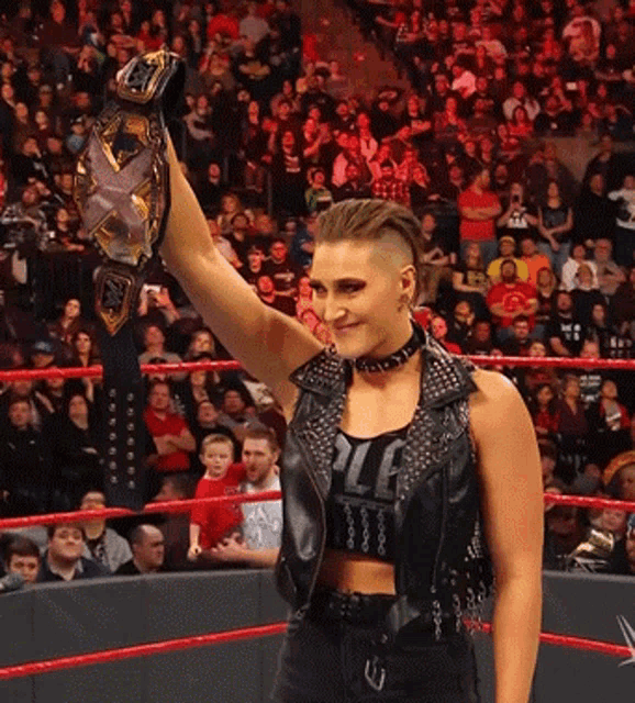 a woman in a wrestling ring holds up a champion 's belt in front of a crowd