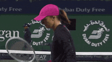 a woman in a pink hat is playing tennis in front of a sign that says dubai duty free