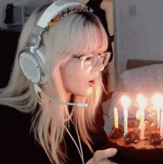 a woman wearing headphones and glasses holds a birthday cake with lit candles