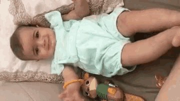 a baby in a blue outfit is laying on a bed next to a stuffed animal .