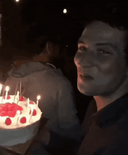 a young man sitting in front of a birthday cake with candles
