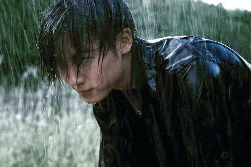 a man in a black jacket is standing in the rain looking down