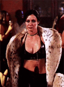 a woman wearing a fur coat and a black top is standing in a room .