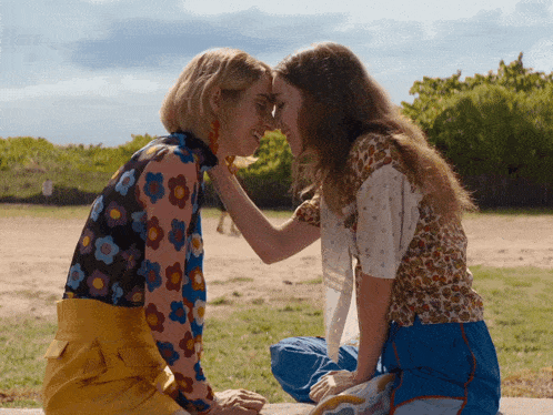 two women are touching their foreheads while sitting on a sidewalk