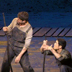 a man in overalls is standing next to another man in overalls on a stage