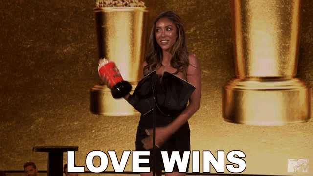 a woman in a black dress is holding a trophy with the words love wins above her