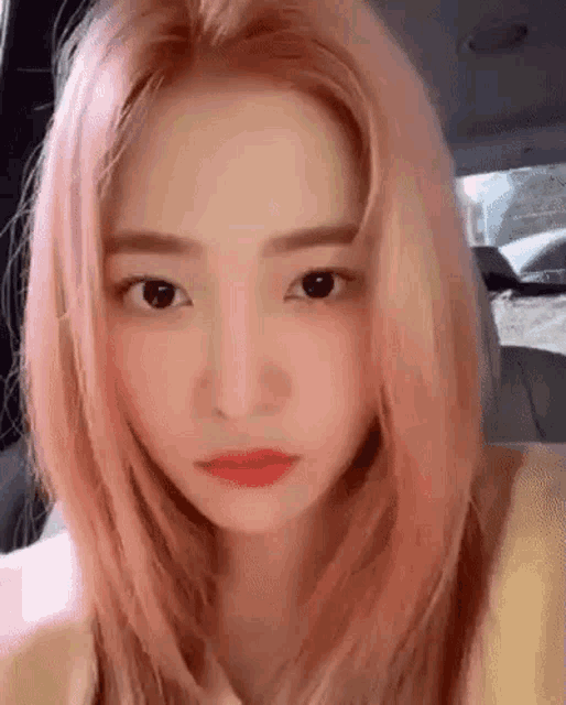 a woman with pink hair is sitting in a car looking at the camera .
