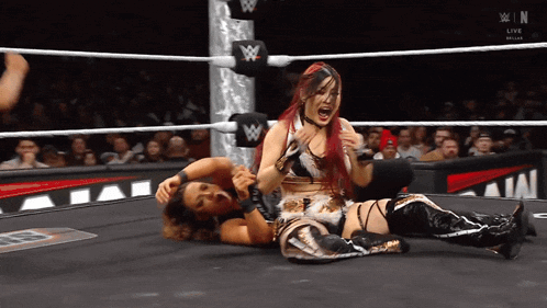 two women wrestling in a ring with a w logo on the ring