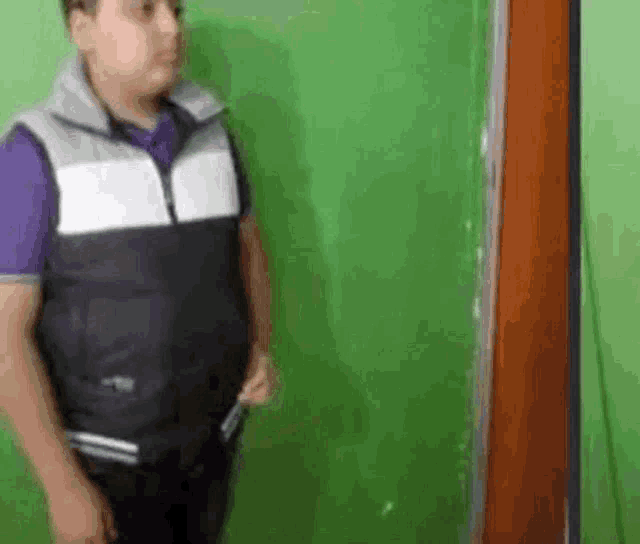 a man in a vest is standing in front of a green wall holding a knife .