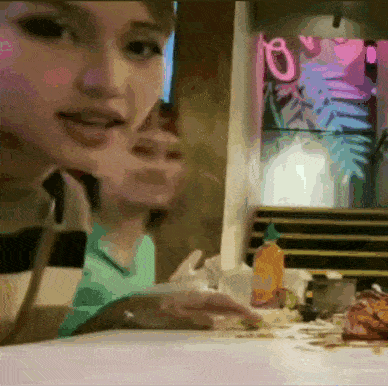 a woman in a green shirt is sitting at a table with a bottle of sauce on it
