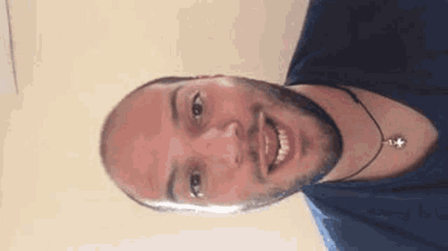 a man with a beard and a necklace is smiling and looking at the camera .