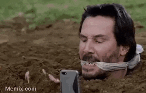 a man is laying in the dirt with his mouth tied and looking at a cell phone .