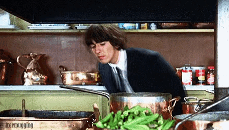 a man in a suit and tie is cooking in a kitchen with a pot of green beans in the foreground