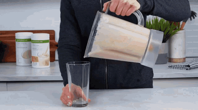 a man pouring a shake into a glass with a bottle of herbalife in the background