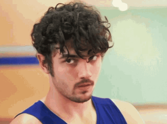 a young man with curly hair and a beard is wearing a blue tank top