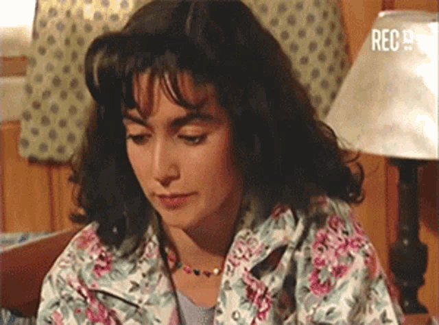 a woman in a floral jacket is sitting in front of a lamp with the word rec on it