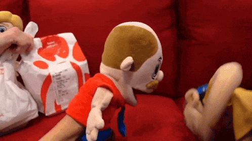 two stuffed animals are sitting on a red couch next to a bag of chicken