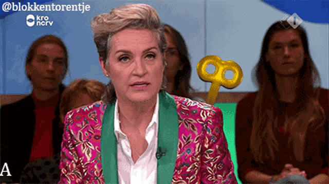 a woman in a pink and green jacket is sitting in front of a group of people