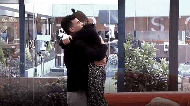 a man and a woman are hugging in front of a window with the letter s on it
