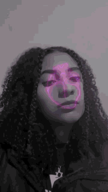 a black and white photo of a girl with curly hair and a glowing heart on her face .