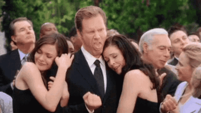 a man in a suit and tie is hugging two women at a wedding .
