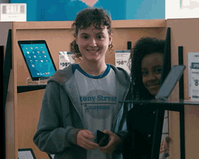 a woman wearing a tony stream shirt holds a phone
