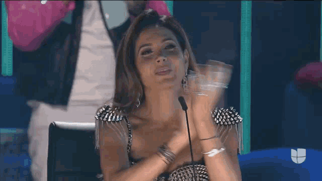 a woman is sitting in front of a microphone and holding a glass of water .