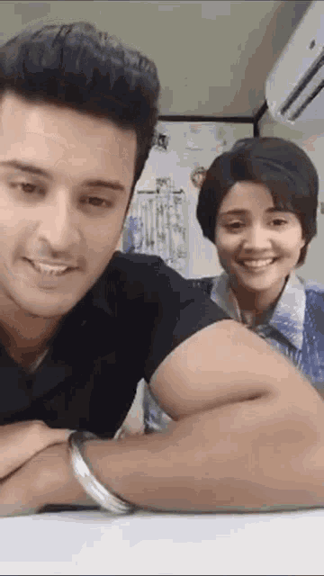 a man and a woman are sitting at a table with their arms crossed and smiling .