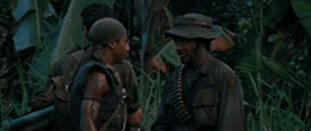 three soldiers are standing in the jungle talking to each other .