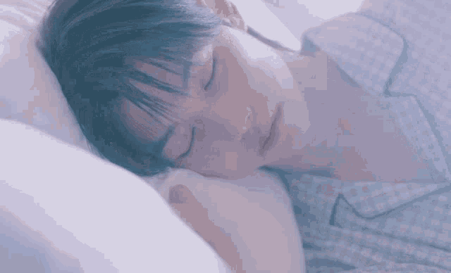 a young man is sleeping in a bed with his eyes closed and a pillow .