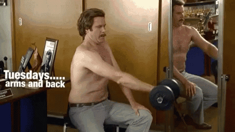 a shirtless man is lifting a dumbbell in front of a mirror and says tuesdays ... arms and back .