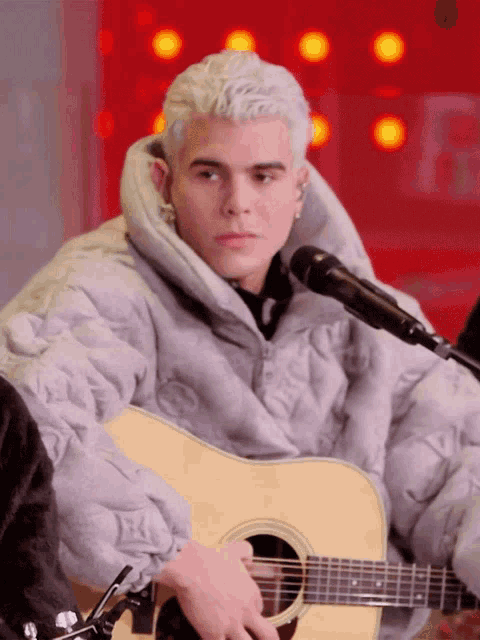 a man in a louis vuitton jacket is playing an acoustic guitar in front of a microphone