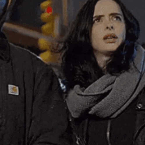 a woman wearing a scarf and a black jacket is standing next to a man .