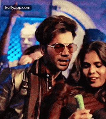 a man wearing sunglasses is standing next to a woman holding a green object .