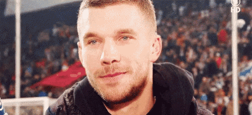 a man with a beard is smiling in front of a crowd of people at a soccer game .