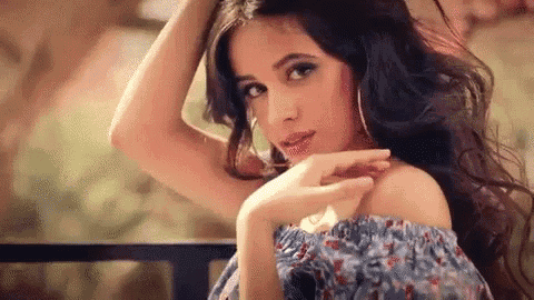 the woman is wearing a blue off the shoulder dress and earrings .
