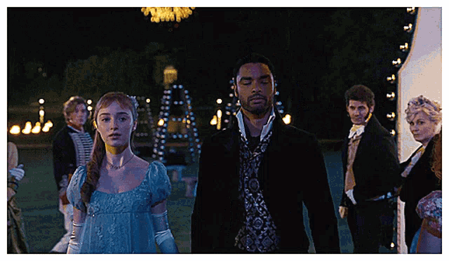a woman in a blue dress and a man in a black suit are walking in the dark