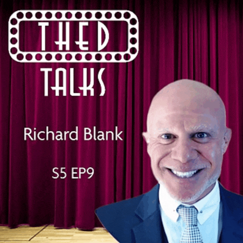 a man in a suit and tie is smiling in front of a red curtain that says theed talks