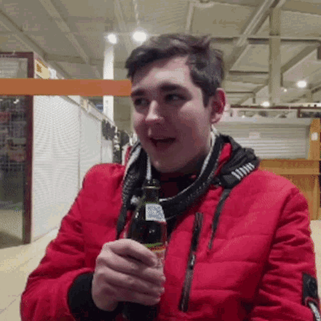 a young man in a red jacket is holding a bottle of soda