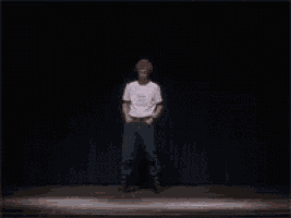 a man in a white t-shirt is standing on a stage