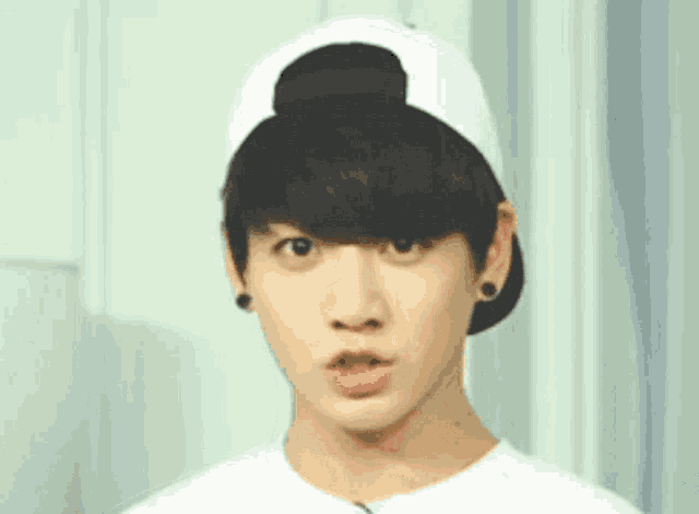 a young man wearing a white baseball cap and a white shirt is making a funny face .