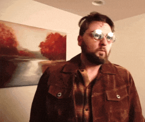 a man wearing sunglasses and a plaid shirt is standing in front of a painting