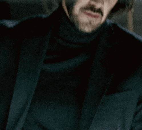 a man with long hair and a beard is wearing a black turtleneck sweater