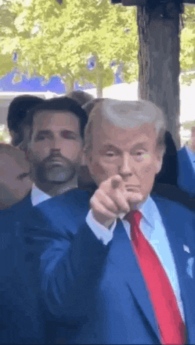 a man in a suit and tie is pointing at the camera while another man stands behind him .