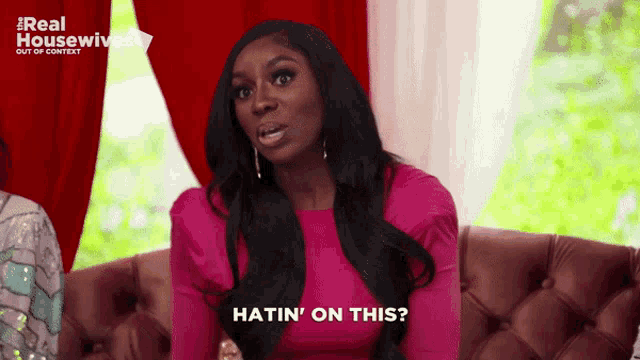 a woman in a pink dress is sitting on a couch and says ' hatin ' on this '